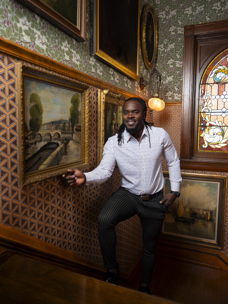 Richard Ferguson adjusting a framed painting on a Victorian staircase elaborately wallpapered wall